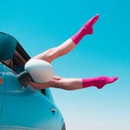 A person wearing pink compression socks with legs dangling out a car window