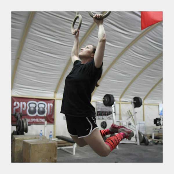 The image shows a person performing a kippling pull up, with each hand on a suspended metal loop.