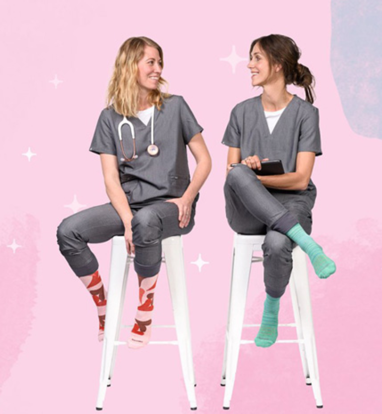 Two nurses chatting while sitting on a chair, wearing scrubs and both wearing compression socks of   different color and design. 