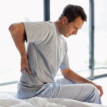 man getting out of bed and experiencing back pains