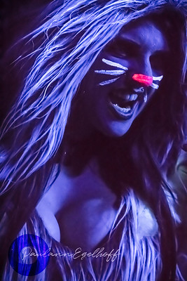 a person in cat costume with facial markings made from blacklight paint which is made visible because of the effects of black lights