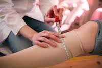 A female measuring the leg of a client for her compression socks.