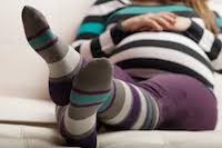 A pregnant woman wearing black and purple striped compression socks.