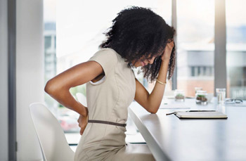 an African American woman seated at her desk and massaging her back