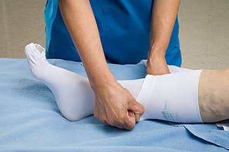 nurse in blue scrub taking off tedhose stocking