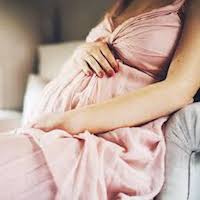 Pregnant woman in a pink dress, resting her hands on her baby bump.