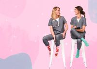 two nurses seated while chatting and showing off their brightly colored compression socks