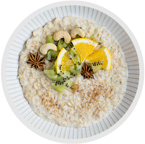 a plate of oatmeal garnished with nuts, star anise, kiwi, and orange wedges