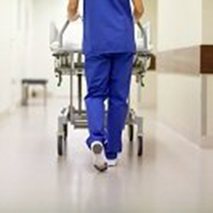 A nurse pushing a hospital bed, wearing scrubs and possibly wearing compression socks while on his shift