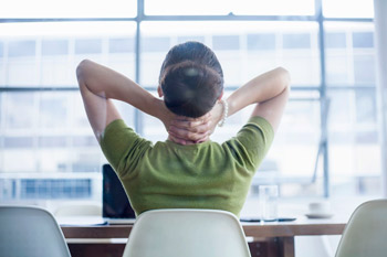 a woman holds her neck to do some stretches while seated at her desk
