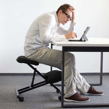 tall man sitting at his deck in a hunched position over his tablet