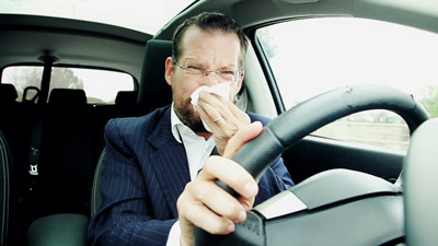 Man sneezing in a car. He should be using a car air purifier like the premium CocoCube Car Air Purifier with 2 HEPA filters. He could even use an iqair car air purifier with 1 HEPA filter. A car air purifier would relieve his allergies by filtering allergens directly out of the air.
