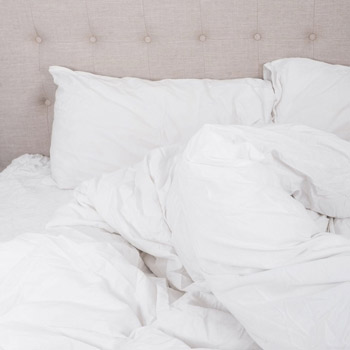 A bed with some white linen including a duvet pushed to one side