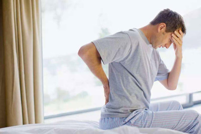 A man sitting in bed holding his head and back